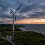 Wind turbine near coastline during sunset with cloudy sky